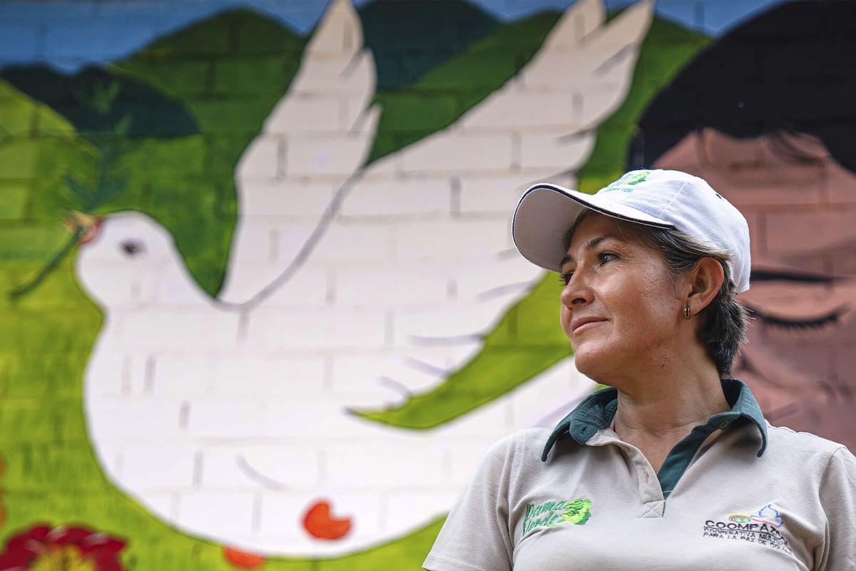 A woman stands in front of a painting of a dove. 